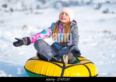 Kleines Mädchen, das draußen auf Tubing-Schnee sitzt und meditiert Stockfoto