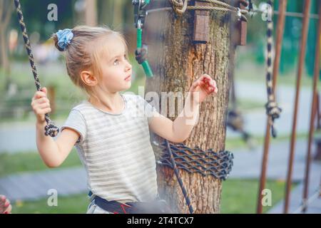 Niedliches Mädchen, das Aktivitäten in einem Kletterpark genießt. Das Mädchen geht auf die Scharnierspur. Stockfoto