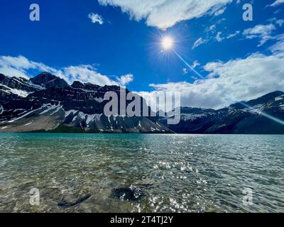 Eine atemberaubende Landschaft eines smaragdgrünen Sees, umgeben von majestätischen Bergen, die in goldenes Sonnenlicht getaucht sind Stockfoto