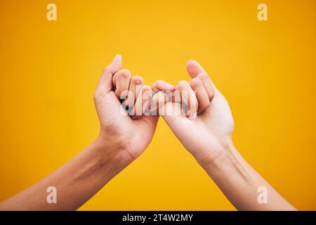 Menschen, Hände und kleine Versprechen im Studio mit Vertrauen, Hilfe oder Hoffnung auf Versöhnung auf gelbem Hintergrund. Finger, Emoji und Deal von Freunden mit Stockfoto