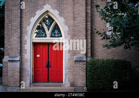 Rote Kirchentür mit gewölbtem Buntglasfenster. Stockfoto