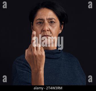 Porträt, Wut und ältere Frau mit Mittelfinger, Meinung und Ausdruck auf schwarzem Atelierhintergrund. Gesicht, weibliche Person und altes Model mit Stockfoto