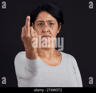 Porträt, Ablehnung und ältere Frau mit Mittelfinger, Meinung und wütendem Ausdruck auf schwarzem Atelierhintergrund. Gesicht, weibliche Person oder älteres Modell Stockfoto