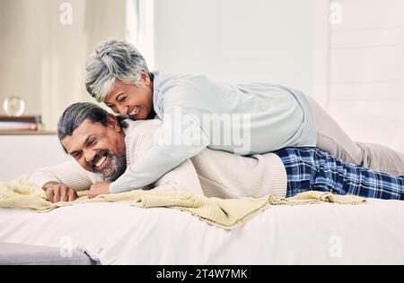 Umarmen, lachen oder ein altes Paar im Schlafzimmer zum Entspannen, Romantik oder einen gemeinsamen Morgen zu Hause. Vertrauen, ältere Frau oder glücklicher älterer Mann, der lügt oder Stockfoto
