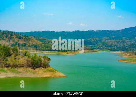 Ein ruhiger, von Menschen geschaffener See, umgeben von majestätischen Hügeln, der den blauen Himmel und die weißen Wolken darüber reflektiert Stockfoto