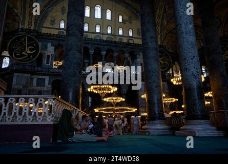 Besucher sitzen, ruhen und beten in der Hagia Sophia, umgeben von Geschichte und Ruhe auf dem emblematischen türkisfarbenen Teppich. Stockfoto