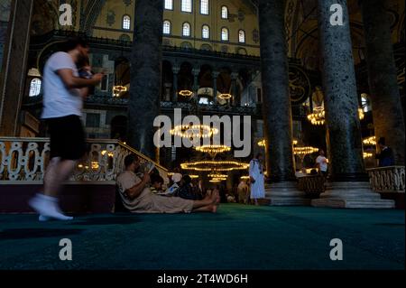 Besucher sitzen, ruhen und beten in der Hagia Sophia, umgeben von Geschichte und Ruhe auf dem emblematischen türkisfarbenen Teppich. Stockfoto