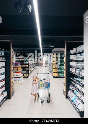 Budva, Montenegro - 01. november 2023: Kleines Mädchen mit Wagen steht in einem Supermarkt in der Nähe von Shampoos und Pflegeprodukten Stockfoto