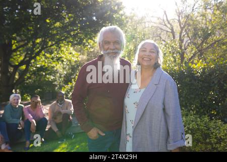 Glückliches birassisches Paar älterer Freunde, die sich umarmen und im sonnigen Garten lächeln Stockfoto