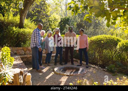 Glückliche, vielfältige Gruppe von älteren Freunden, die im sonnigen Garten stehen und lächeln Stockfoto