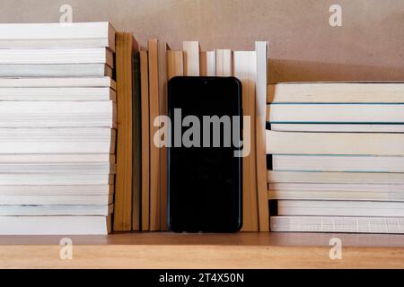 Stapel Bücher auf hölzernem Bücherregal mit leerem Bildschirm-Smartphone in der Mitte. Bildungs- und Wissenskonzept Stockfoto