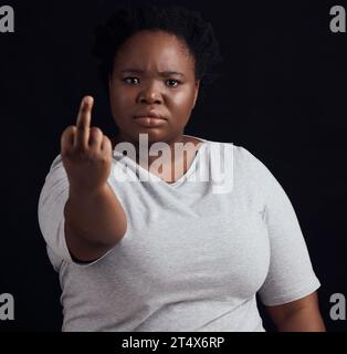Porträt, Wut und schwarze Frau mit Mittelfinger, Meinung und wütendem Ausdruck auf dunklem Studiohintergrund. Gesicht, weibliche Person und afrikanisches Modell Stockfoto