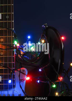 Alte gebrauchte Vintage-E-Gitarre mit Weihnachtslichtern auf dunkelblauem Hintergrund Stockfoto