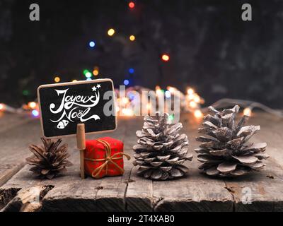 Kleine Tafel mit der französischen Inschrift Frohe Weihnachten auf einem Holztisch, verschwommene Weihnachtslichter im Hintergrund Stockfoto