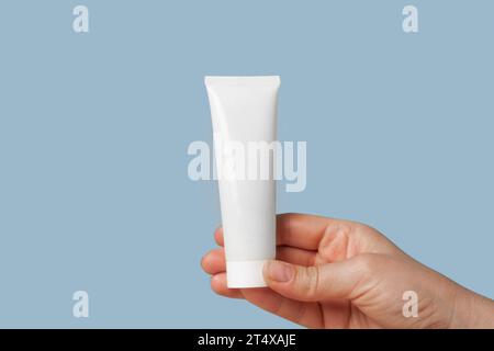 Weiße Creme-Verpackungsschablone in weiblicher Hand. Blauer Hintergrund. Naturkosmetik Zeigen. Mockup Für Schönheitsprodukte. Hautpflege, Gesichtsmaske, Toner. Vorn Vi Stockfoto