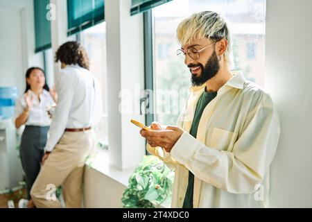 Ein lächelnder junger Mann benutzt das Telefon in einem Coworking Stockfoto