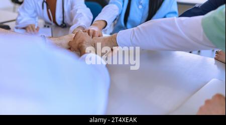 Eine Gruppe von Ärzten und einer medizinischen Krankenschwester vereinen ihre Hände auf einem Tisch und zeigen die unerschütterliche Teamarbeit und Solidarität, die sie antreibt Stockfoto