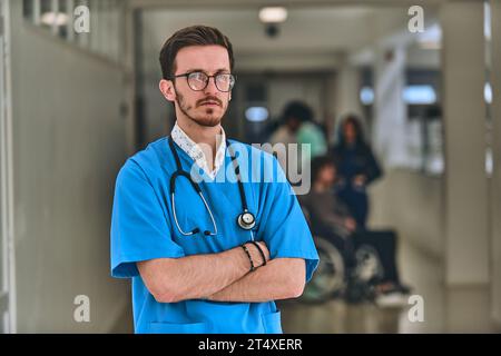 Ein Arzt steht souverän in einem Krankenhausflur mit überkreuzten Armen und strahlt Entschlossenheit und Professionalität im klinischen Umfeld aus. Stockfoto