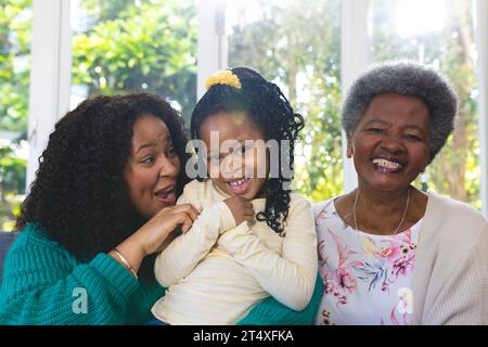 Glückliche afroamerikanische Mutter, Tochter und Enkelin, die zu Hause auf der Couch sitzen, Kopierraum Stockfoto