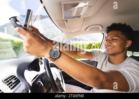 Glücklicher afroamerikaner, der den Rückspiegel im Auto an sonnigen Tagen einstellt Stockfoto