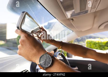 Hände eines afroamerikanischen Mannes, der den Rückspiegel im Auto an sonnigen Tagen justiert Stockfoto