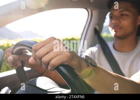 Glücklicher afroamerikaner mit Händen am Lenkrad, der an sonnigem Tag Auto fährt Stockfoto