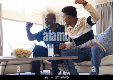 Aufgeregt afroamerikanischer Vater und erwachsener Sohn, der Sport im fernsehen sieht und den Sieg feiert Stockfoto
