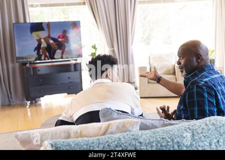 Glücklicher afroamerikanischer Vater und erwachsener Sohn, der Sport im fernsehen sieht und spricht Stockfoto
