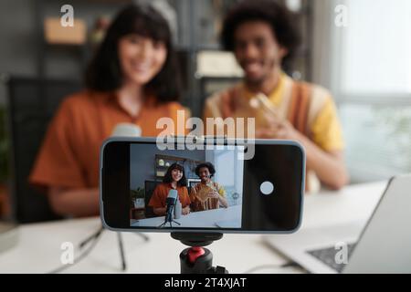 Bildschirm eines Smartphones mit zwei jungen interkulturellen Bloggern und Kunden, die dem Publikum unverpackte Waren zeigen, die im Online-Shop bestellt wurden Stockfoto