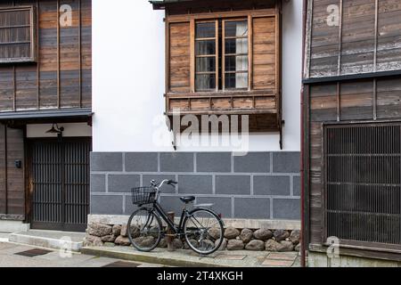 Blick auf die städtische Straße auf die Fassade eines typisch japanischen Hauses mit modernen Stein- und traditionellen Holzfenster und Türen und Fahrrad, das vor dem Haus geparkt ist Stockfoto
