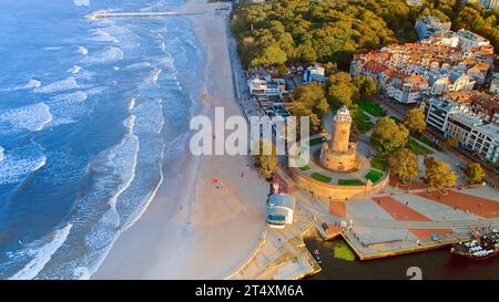 Das Drohnenfoto fängt Kołobrzeg maritimen Charme mit dem berühmten Leuchtturm, dem braunen Meer, turbulenten Wellen, einem entfernten Pier und herbstlichen Farbtönen ein Stockfoto