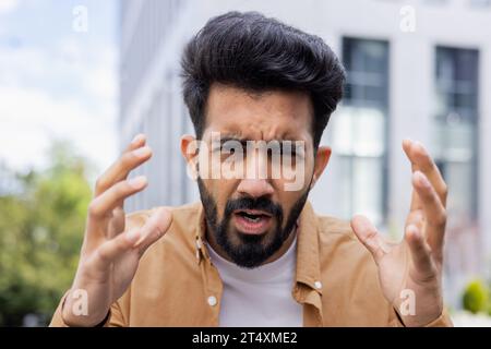 Ein wütender und schreiender Mann aus der Nähe des klingelnden Bürogebäudes schaut nervös in die Kamera, während er in Hemd in der Stadt spaziert. Stockfoto
