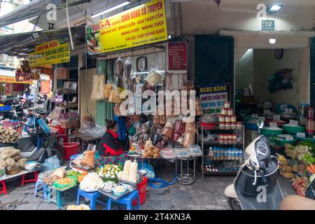 Hanoi, Vietnam, 30. März 2023; Straßenverkäuferin sitzt auf einem Hocker ihres Ladens in einem der Viertel der Stadt und verkauft grundlegende Lebensmittel und Lebensmittel Stockfoto