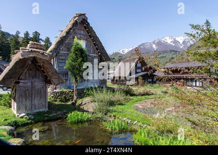 Shirakawa Go, Japan-20. April 2023: Flacher Blick auf Bauernhäuser mit traditionellen Strohdächern des Dorfes mit schneebedeckten Bergen im Hinterland Stockfoto