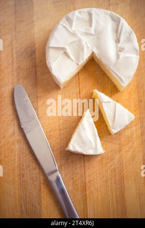 Camembert-Käse mit einer Dreiecksscheibe und einem Messer auf einem Holzbrett Stockfoto