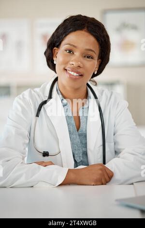 Schwarze Ärztin an ihrem Schreibtisch, glücklich und sitzend in ihrem Büro in einer Klinik oder einem Krankenhaus. Erfolg, Arbeit und ein Lächeln, junge weibliche Gesundheitsversorgung Stockfoto