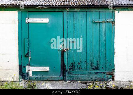 Paar falsch abgestimmte, mit Vorhängeschloss verschlossene Garagentüren aus Holz, die bessere Zeiten gesehen haben Stockfoto