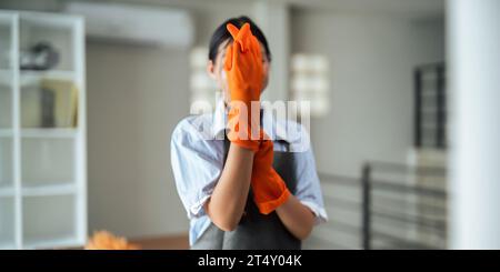 Nahaufnahme einer Dienstmädchen, die Gummihandschuhe mit Chemikalien anzieht und Einrichtungen zum Aufräumen des Reinigungsbüros im Hintergrund Stockfoto