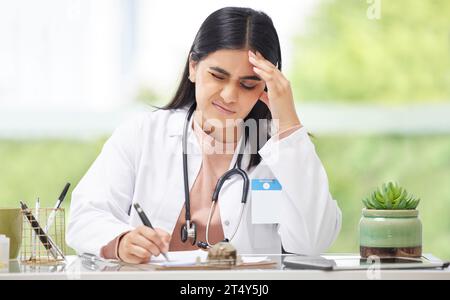 Kopfschmerzen, Stress und Burnout Arzt, der im Krankenhaus arbeitet, Schmerzen schaut und in ein Buch schreibt, während er im Büro in der Klinik sitzt. Müde Stockfoto