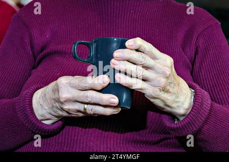 Nahaufnahme einer älteren Frau, die eine Tasse heiß hält Kaffee Stockfoto