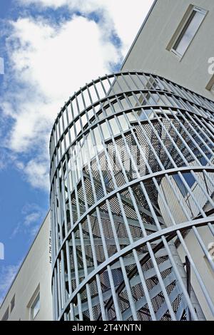 Eine Wendeltreppe an der Außenseite eines Gebäudes. Graue Wendeltreppe aus Stahl an der Seite des modernen Bürogebäudes. Niedriger Winkel eines Metalls Stockfoto