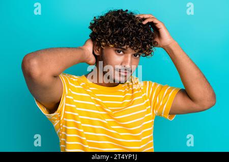 Porträt der schönen kühlen amerikanischen Mann Hände berühren wellige Haare gesunde Haarbehandlung isoliert auf türkisfarbenem Hintergrund Stockfoto