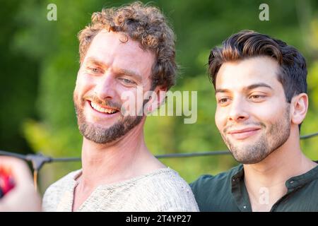 Zwei attraktive junge Millennial-Männer, einer kaukasische und einer mit südeuropäischem Charme, teilen sich einen gemütlichen Moment, während sie posieren und lächeln für ein Foto. Ihr Lächeln spiegelt den Geist der Kameradschaft und die wunderschöne Mischung der Kulturen wider und fängt das Wesen jugendlicher Freundschaft und Inklusivität ein. Fröhliches Millennial Duo lächelt für Snapshot in Unity. Hochwertige Fotos Stockfoto