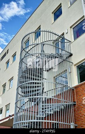 Eine Wendeltreppe, die an der Seite eines Gebäudes verläuft. Notausstieg Notausstieg. Hinterhof-Fluchttreppe. Gekapselte Notleiter für die Sicherheit von Stockfoto