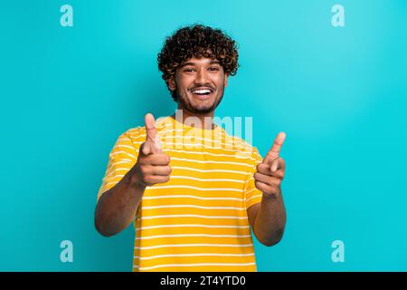 Fotoporträt der schönen jungen männlichen Punktkamera, die Sie kleideten stilvolles gestreiftes gelbes Kleid isoliert auf cyanfarbenem Hintergrund Stockfoto