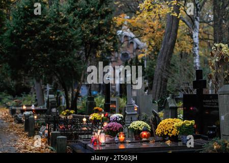 Warschau, Polen. November 2023. Am Allerheiligen auf dem evangelisch-Augsburger Friedhof in Warschau stehen Blumen und beleuchtete Kerzen auf den Gräbern. Allerheiligen (oder Dzie? Zaduszny (Polnisch) ist ein Feiertag in Polen. Es ist eine Gelegenheit, an verstorbene Verwandte zu erinnern. An diesem Tag bringen die Menschen Blumen, typischerweise Chrysanthemen, und Kerzen auf Friedhöfe. Der gesamte Friedhof ist voller Lichter in der Dunkelheit. Der Evangelisch-Augsburger Friedhof ist ein historischer lutherischer evangelischer Friedhof im Westen von Warschau. Seit seiner Eröffnung im Jahr 1792 waren es mehr als 100.000 Menschen Stockfoto