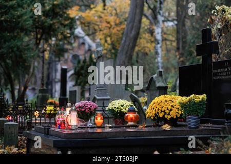 Warschau, Polen. November 2023. Am Allerheiligen auf dem evangelisch-Augsburger Friedhof in Warschau stehen Blumen und beleuchtete Kerzen auf den Gräbern. Allerheiligen (oder Dzie? Zaduszny (Polnisch) ist ein Feiertag in Polen. Es ist eine Gelegenheit, an verstorbene Verwandte zu erinnern. An diesem Tag bringen die Menschen Blumen, typischerweise Chrysanthemen, und Kerzen auf Friedhöfe. Der gesamte Friedhof ist voller Lichter in der Dunkelheit. Der Evangelisch-Augsburger Friedhof ist ein historischer lutherischer evangelischer Friedhof im Westen von Warschau. Seit seiner Eröffnung im Jahr 1792 waren es mehr als 100.000 Menschen Stockfoto