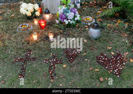 Warschau, Polen. November 2023. Kerzen, Herz und Kreuze aus Kastanien werden am Allerheiligen auf dem evangelisch-Augsburger Friedhof in Warschau auf das Grab gesetzt. Allerheiligen (oder Dzie? Zaduszny (Polnisch) ist ein Feiertag in Polen. Es ist eine Gelegenheit, an verstorbene Verwandte zu erinnern. An diesem Tag bringen die Menschen Blumen, typischerweise Chrysanthemen, und Kerzen auf Friedhöfe. Der gesamte Friedhof ist voller Lichter in der Dunkelheit. Der Evangelisch-Augsburger Friedhof ist ein historischer lutherischer evangelischer Friedhof im Westen von Warschau. Seit seiner Eröffnung im Jahr 1792, mehr als Stockfoto