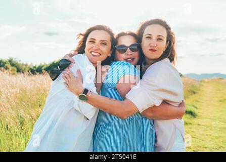Porträt von drei fröhlichen, lächelnden Frauen, die sich beim Wandern im Freien umarmen. Sie starren in die Kamera. Frauenfreundschaft, Beziehungen und Glück Conc Stockfoto