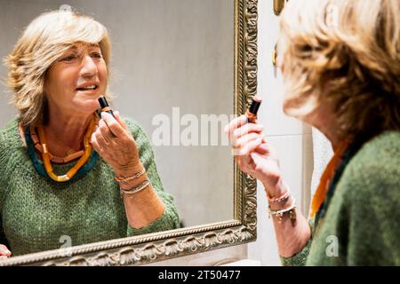 Reife Frau, die ihre Lippen vor dem Badezimmerspiegel macht Stockfoto